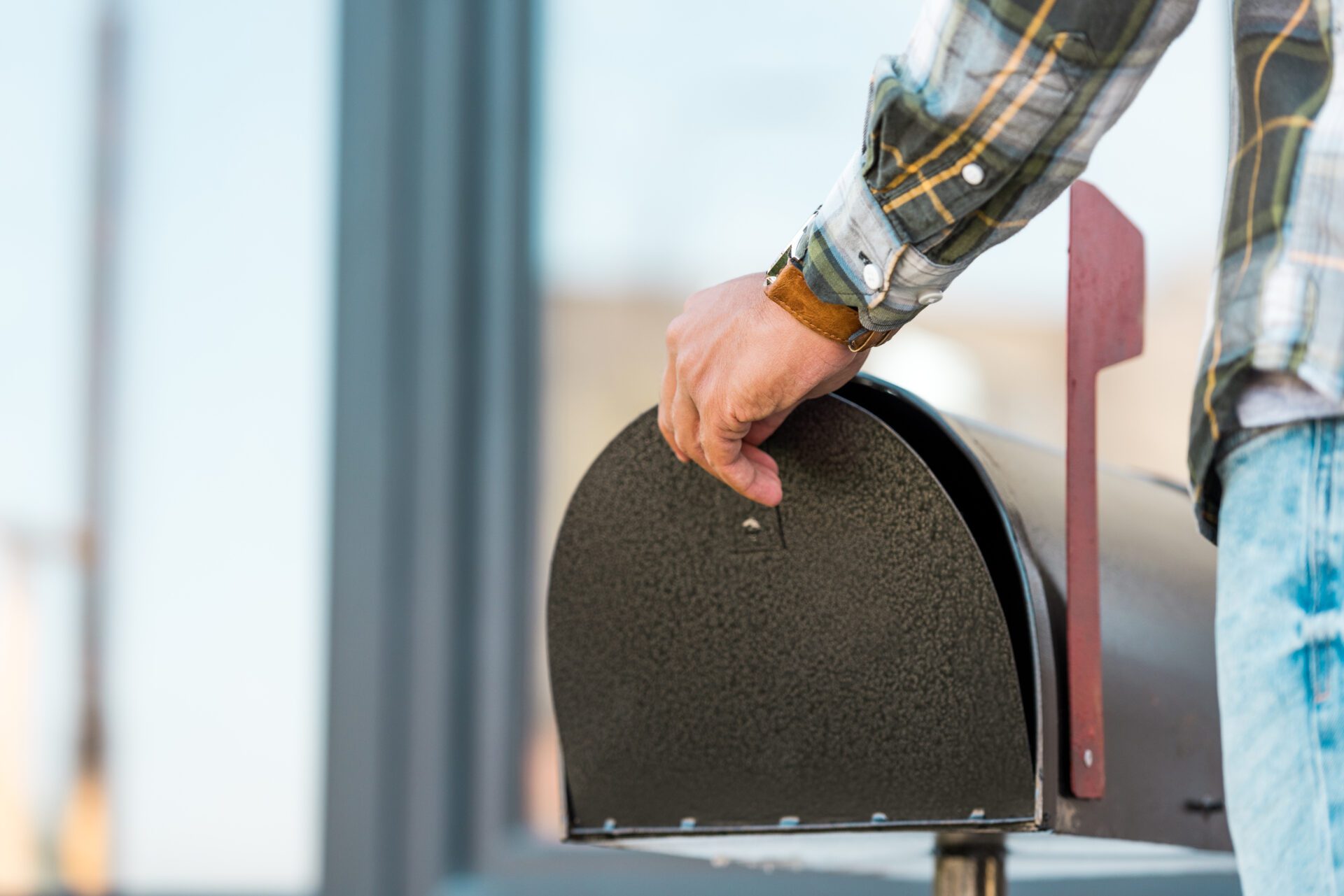 cropped view of man opening black mailbox near house